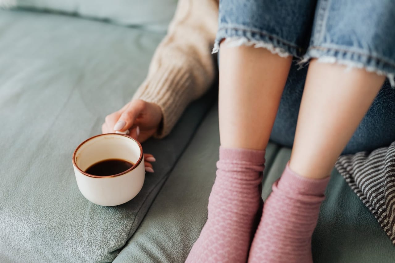 Feet in pink socks on a green sofa beside a hand resting on a cup