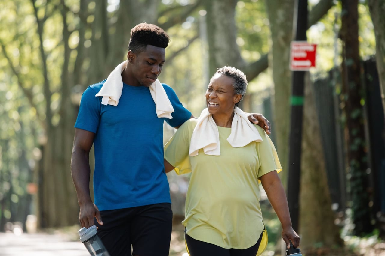 Young man and older woman with towels around their necks walking along a tree-lined sidewalk