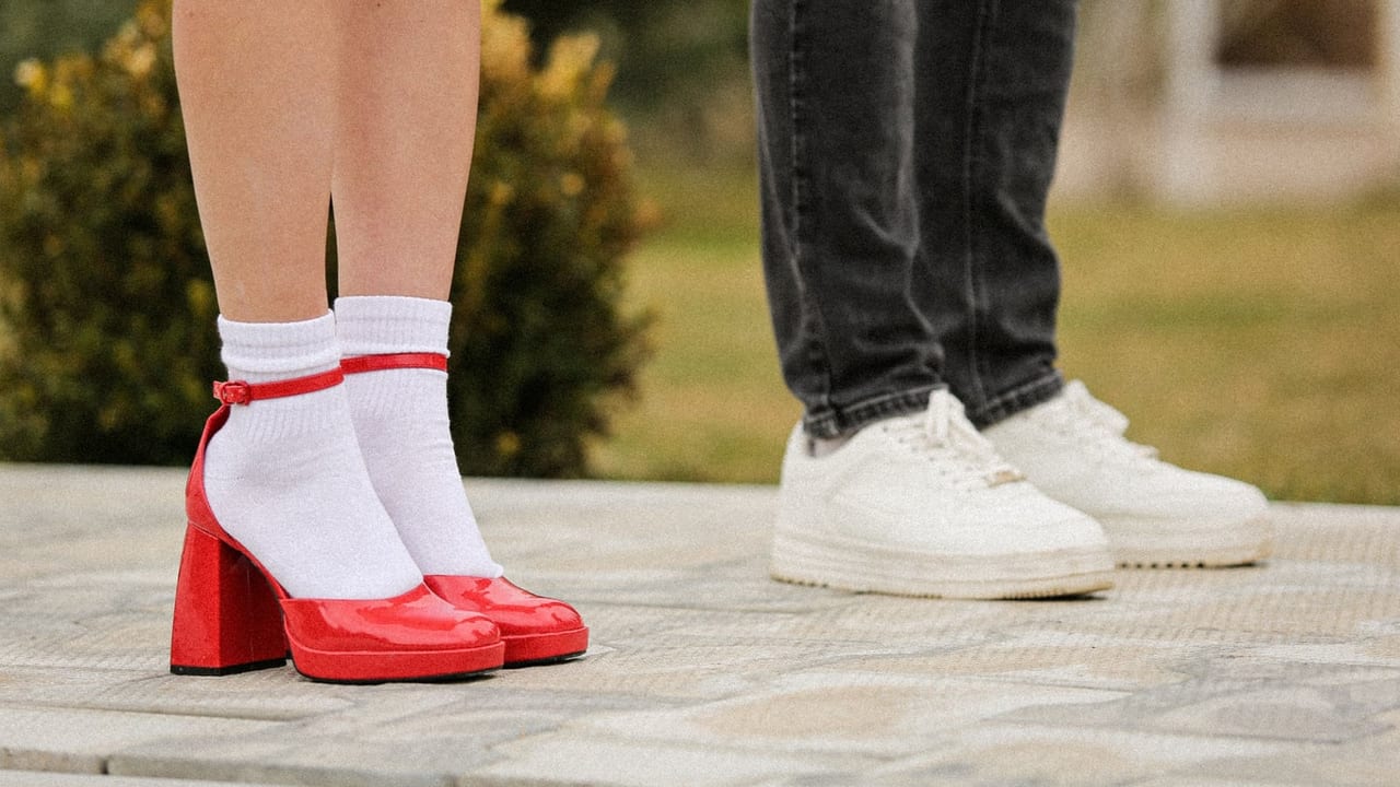 Red block-heel shoes with white socks beside flat white sneakers on stone paving