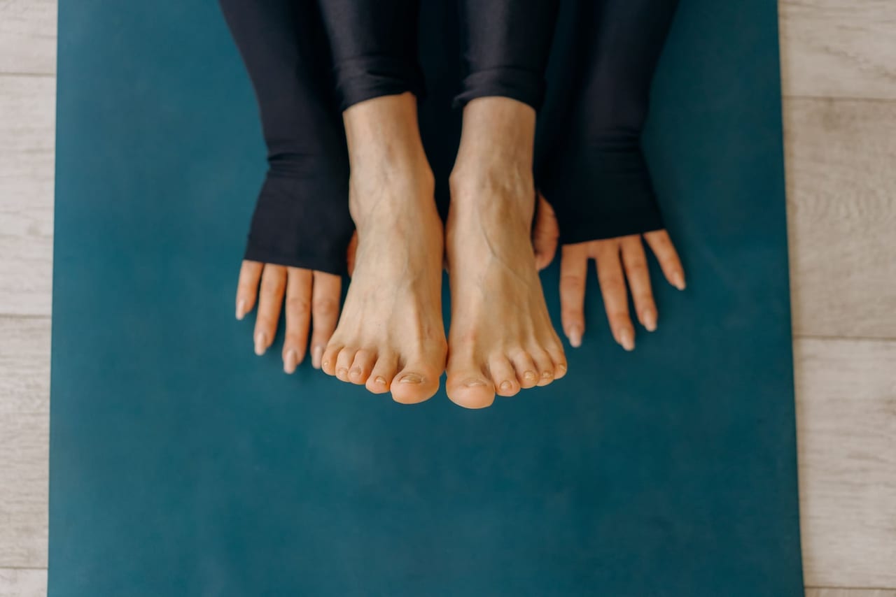 Bare feet side by side on a teal yoga mat, hands resting flat beside them