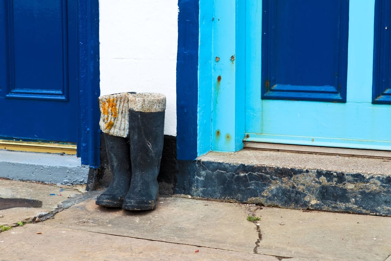 A pair of black rubber boots with knit cuffs standing on the step beside a blue door