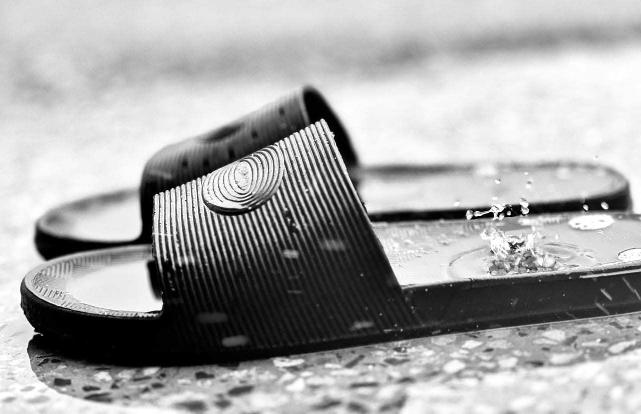 Black rubber slides on a terrazzo floor, water splashing onto a footbed, in black and white