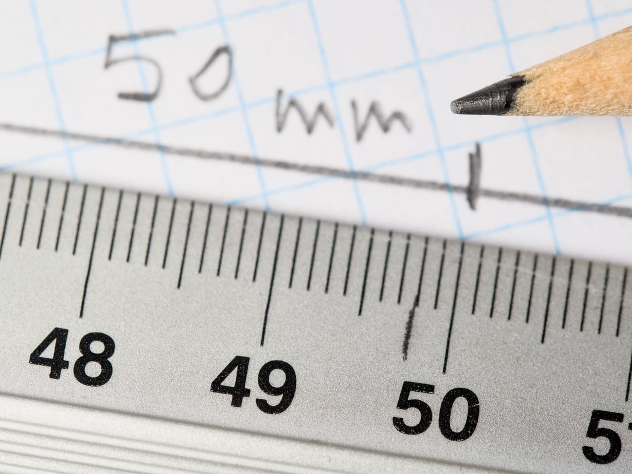 Pencil tip marking a measurement on graph paper above a metal ruler