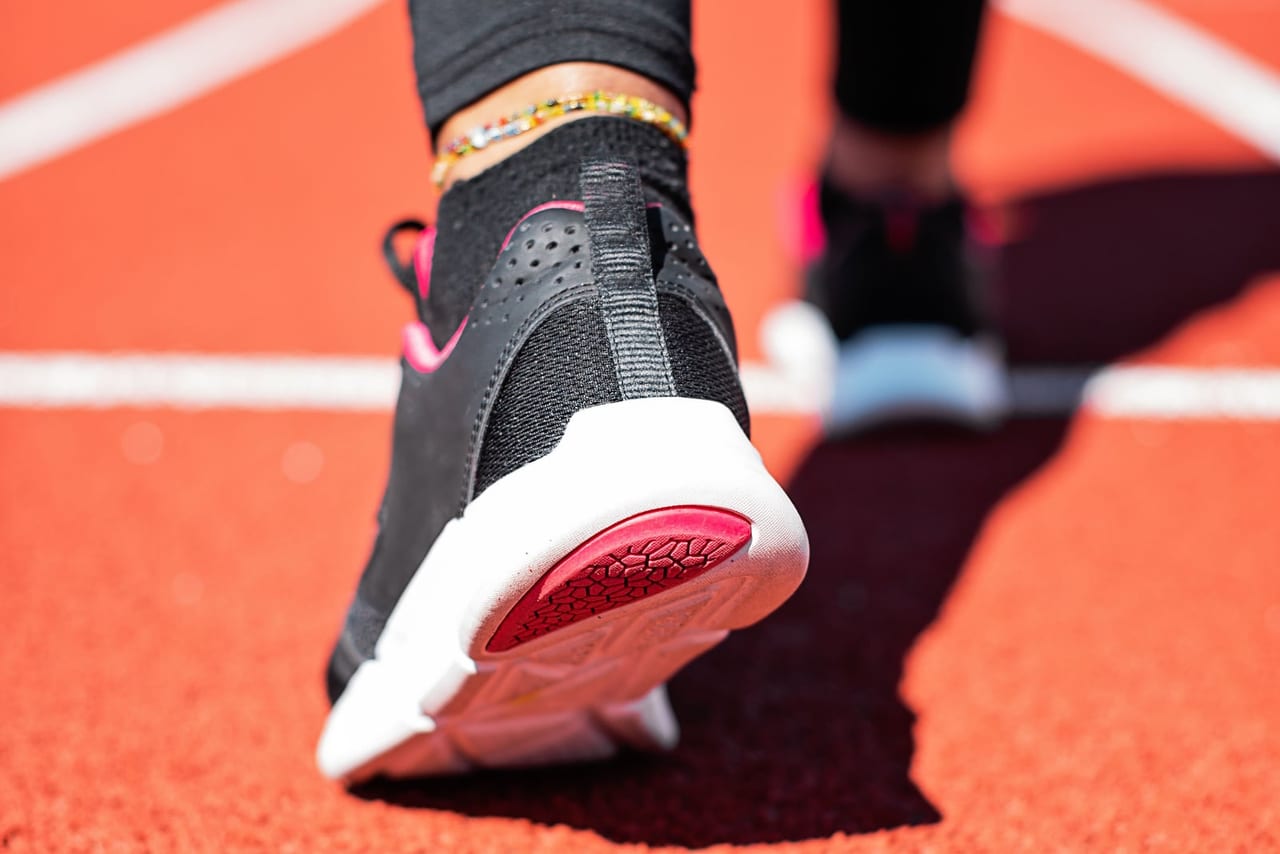 Black running shoe with a pink-accented sole mid-stride on a red running track