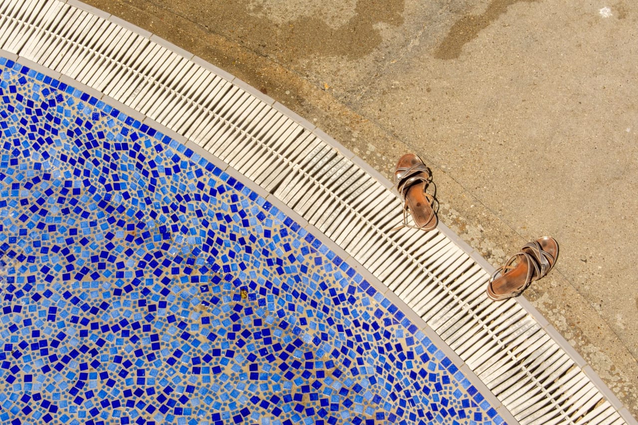 Pair of brown strappy sandals on wet concrete beside a blue mosaic pool edge