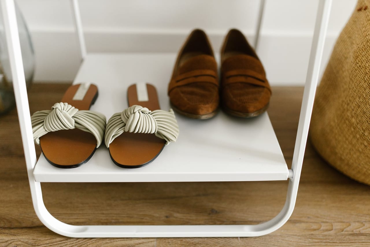 Knotted-strap slide sandals and brown suede loafers on a white open shoe rack