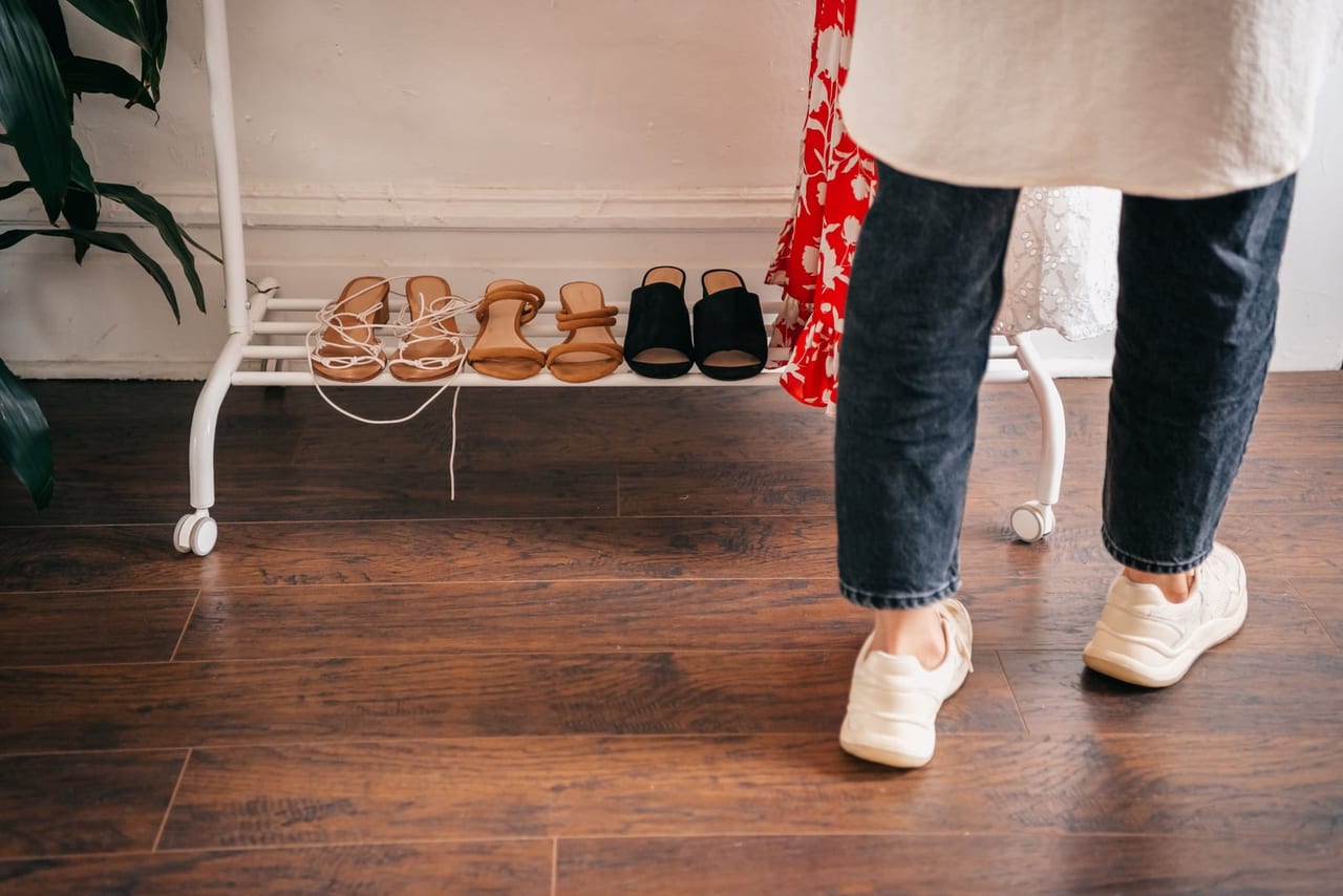 Sandals lined up on a white shoe rack beside a person in jeans and sneakers