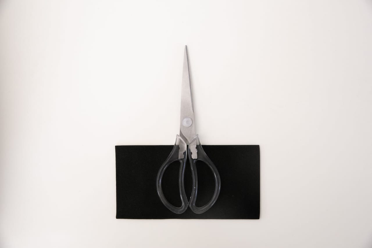 Pair of steel scissors with clear gray handles resting on a black sheet on white