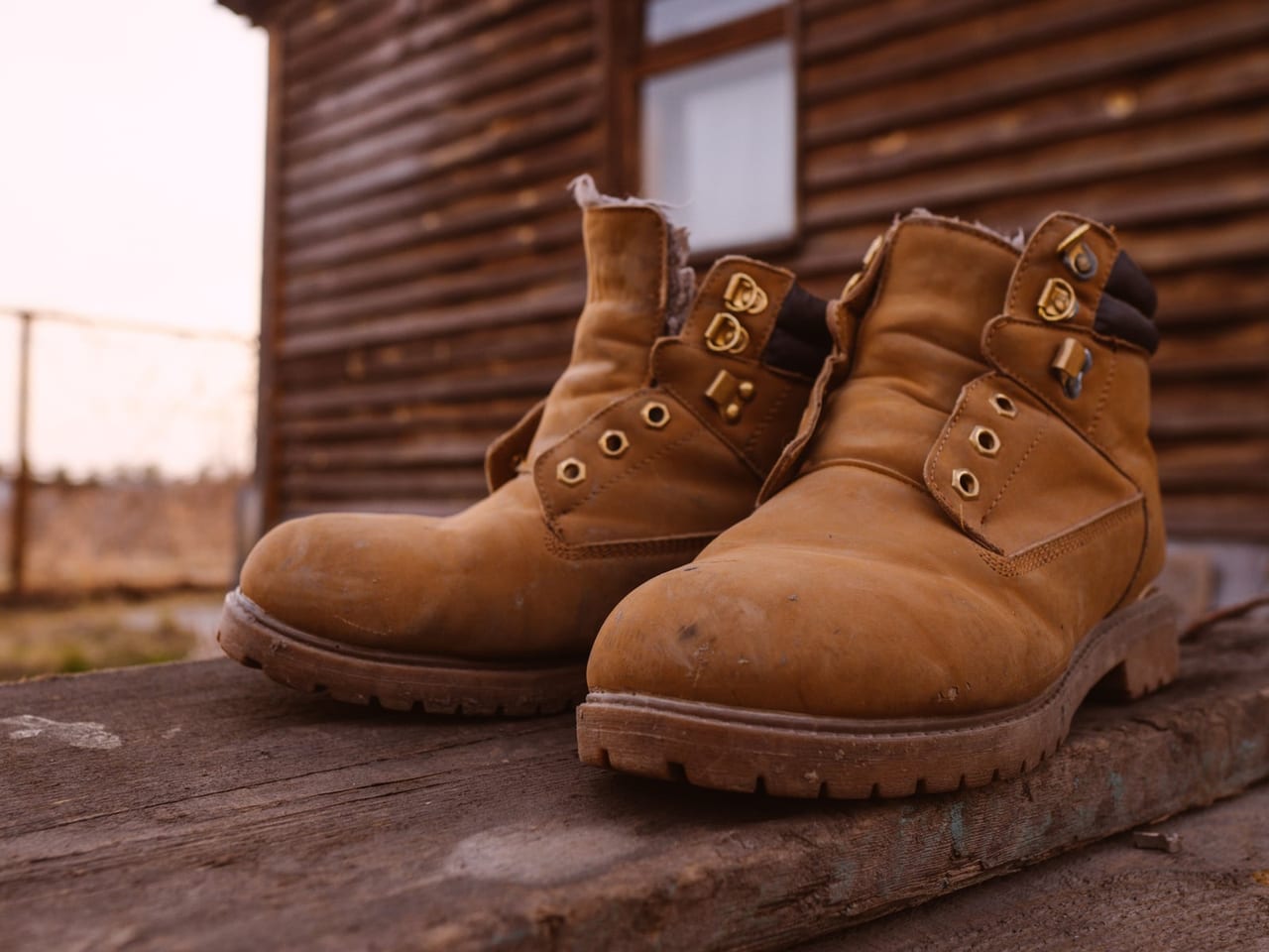 Pair of scuffed, unlaced tan leather work boots on a weathered wooden platform