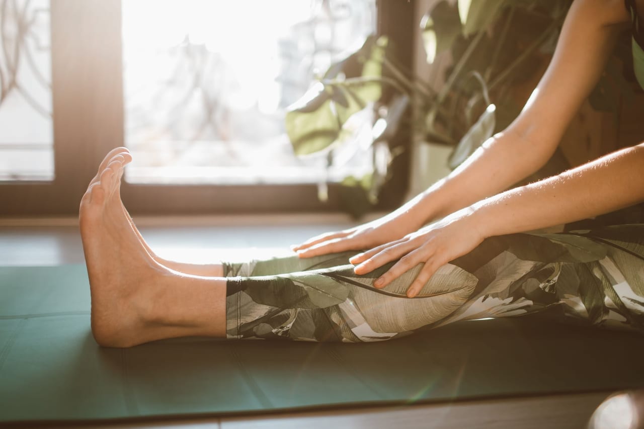 Bare foot of a seated person stretching forward on a mat by a sunny window