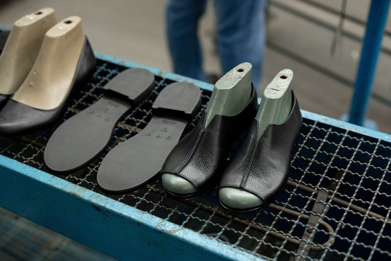 Black soles and half-made leather shoes on lasts on a mesh workshop bench