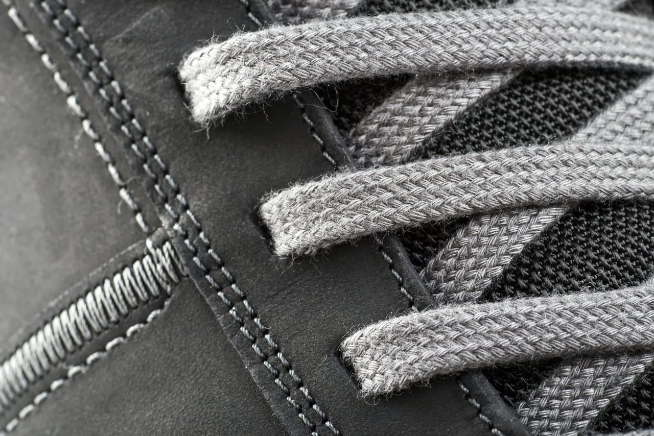 Close-up of flat gray laces crossing through the eyelets of a dark gray shoe