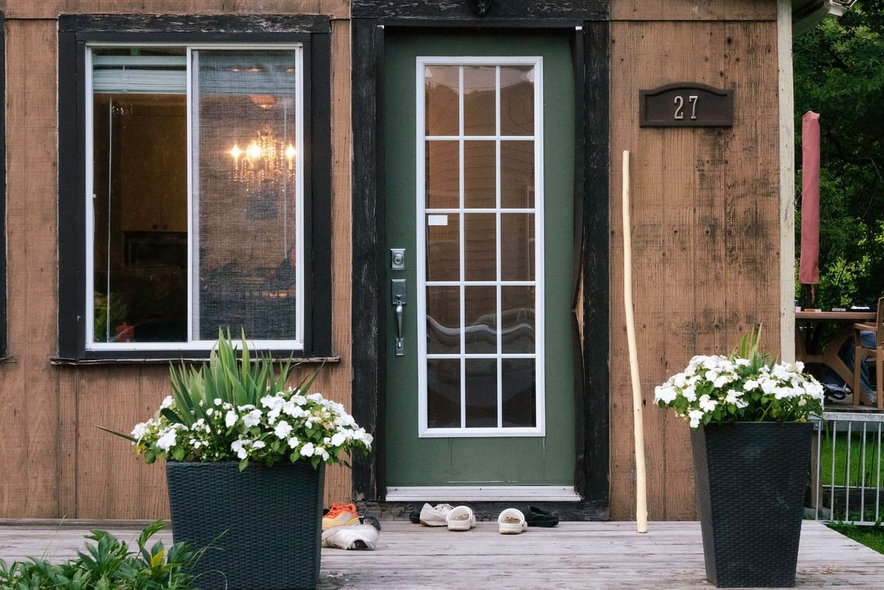 Casual shoes left on a wooden porch below a green front door with potted flowers