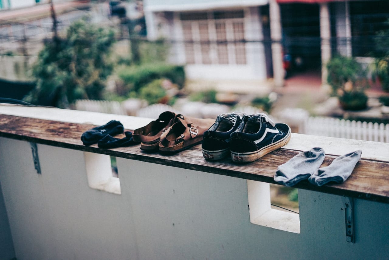 Black sneakers, brown sandals and gray socks set out on a wooden balcony railing