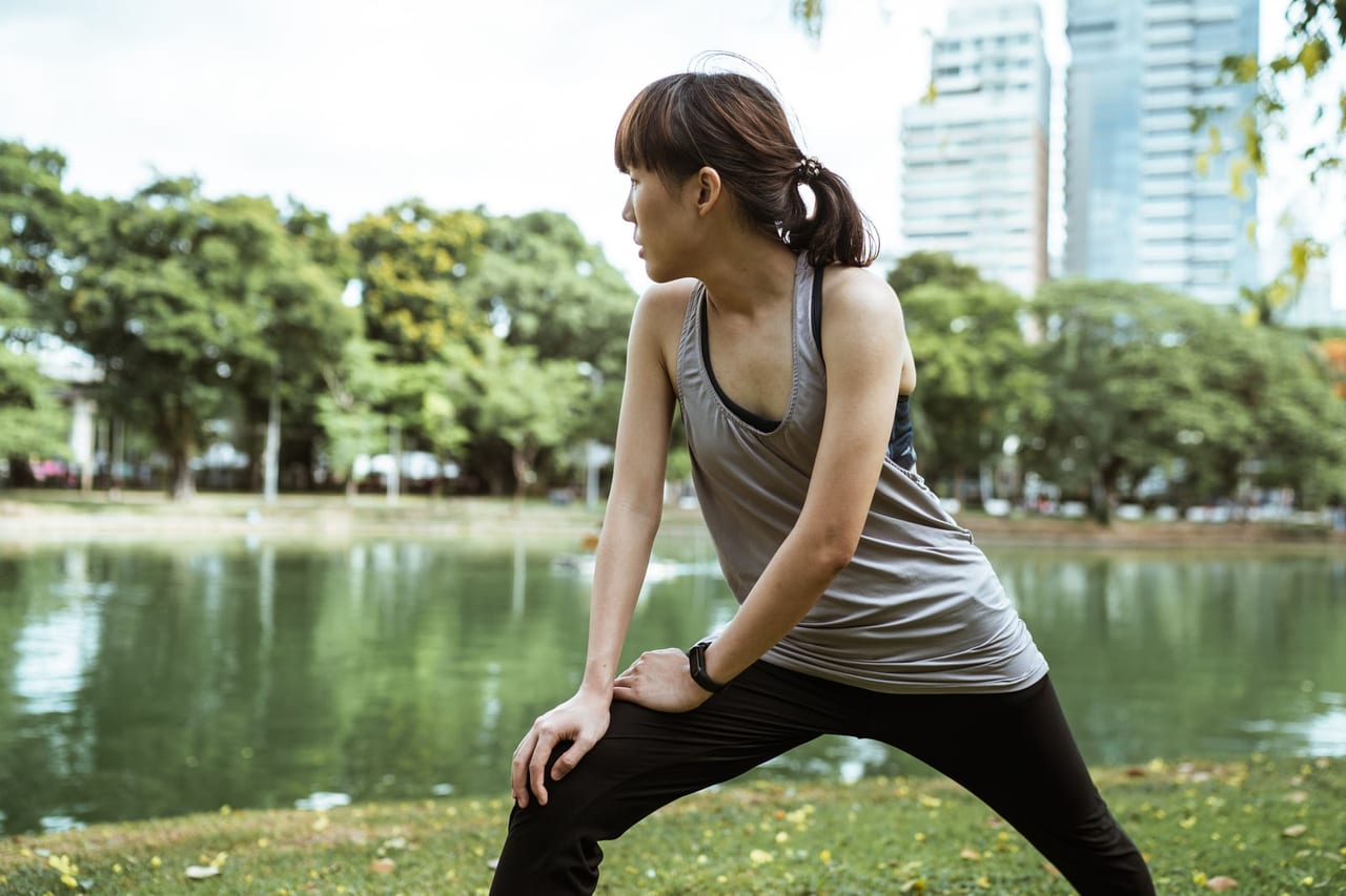 Woman in a gray tank top warming up in a side lunge beside a park lake