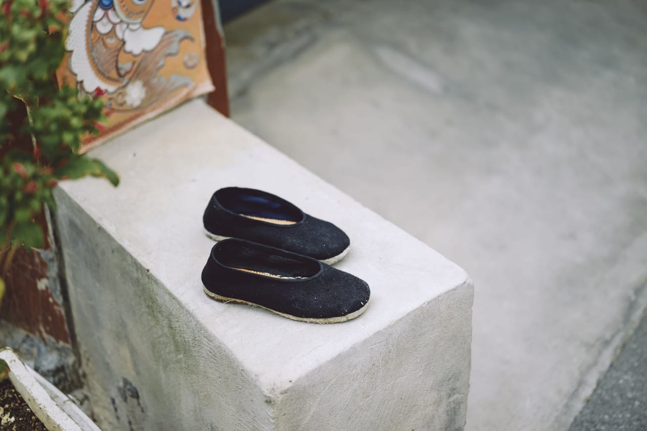 Pair of black cloth slip-on shoes set out on a concrete ledge beside a plant