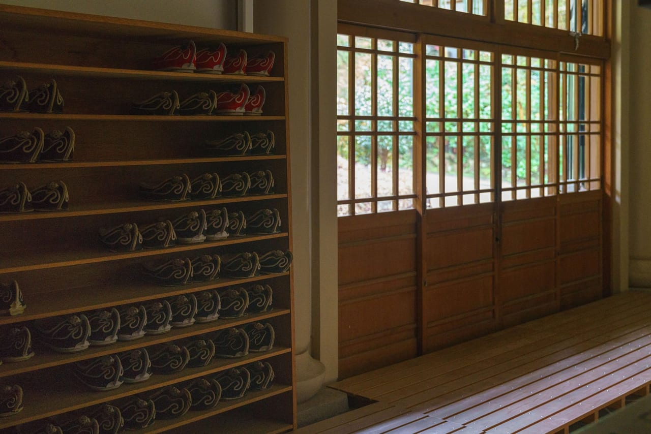 Rows of slippers on wooden shelves beside a bench and sliding windows at an entrance