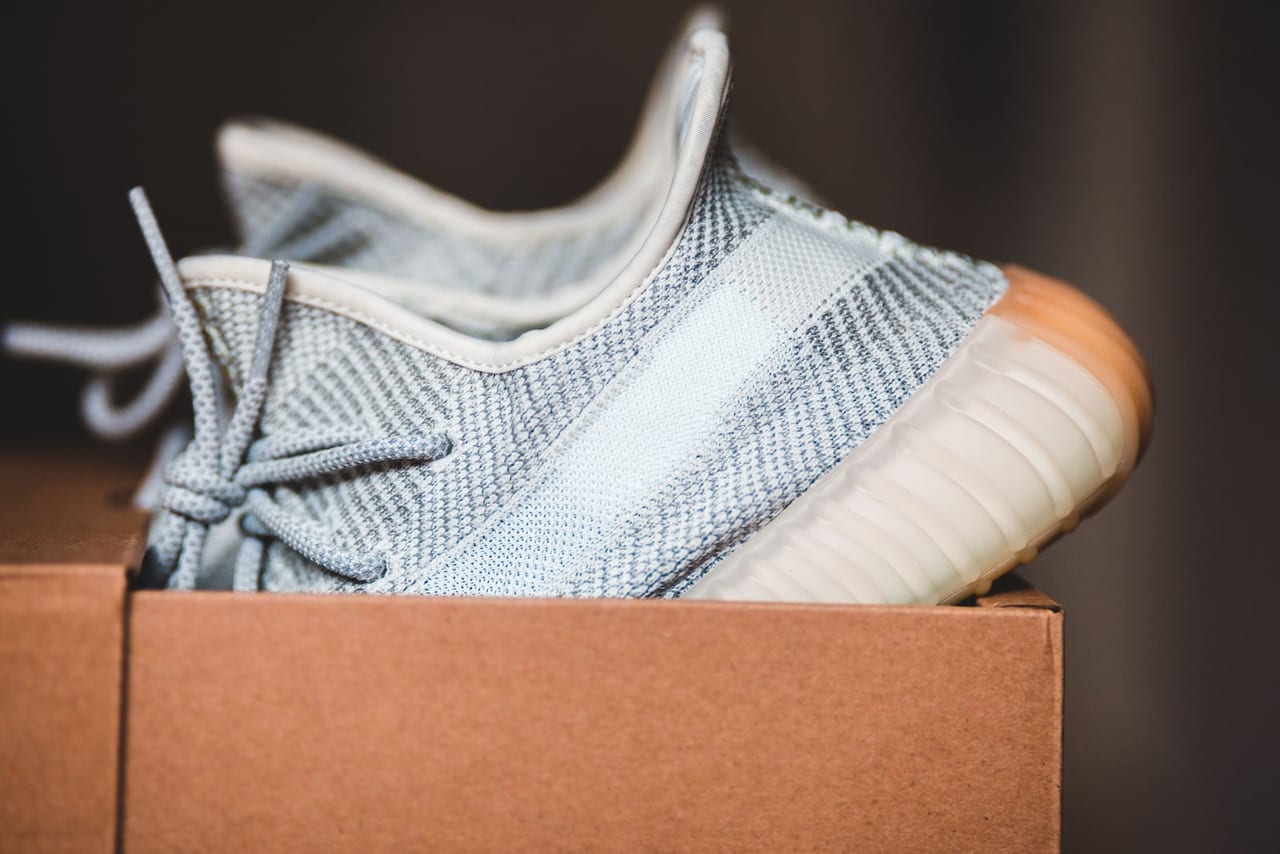 Light gray knit lace-up sneaker resting in an open cardboard shoebox, seen from the side