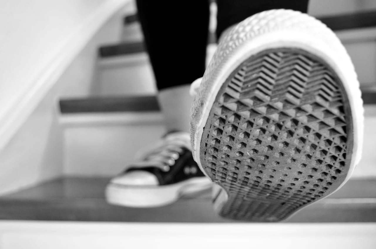 Black-and-white close-up of a sneaker's patterned rubber sole lifted on a staircase