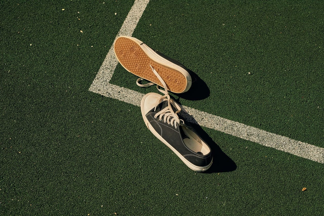 Black canvas sneakers on a green sports field, one flipped over to show its tread