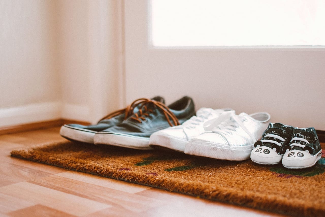 Three pairs of sneakers, including a baby's pair, on a woven doormat by a door