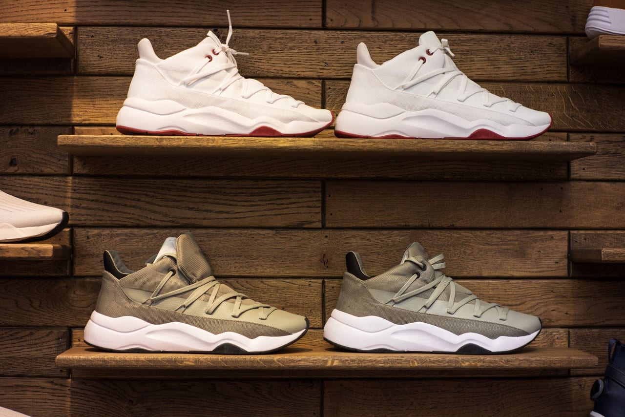 Two pairs of sneakers, one white and one gray, displayed on wooden wall shelves