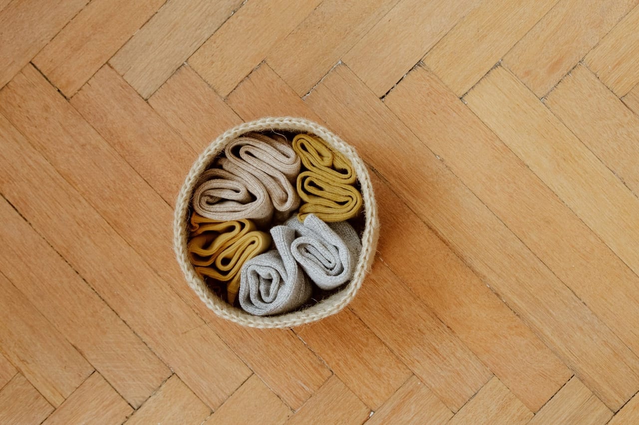 Rolled socks in beige, mustard and gray in a small woven basket on parquet