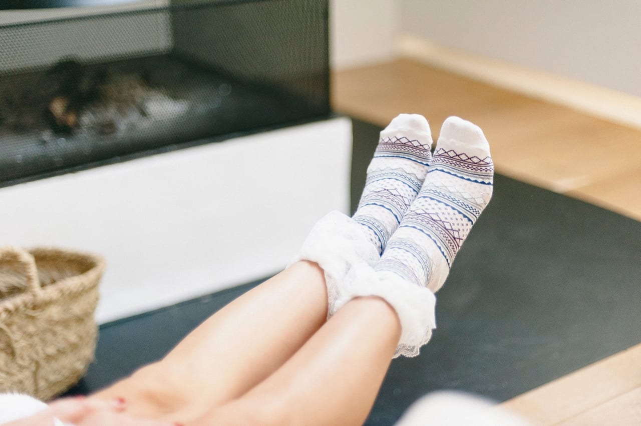 Feet in patterned white socks raised side by side in front of a fireplace