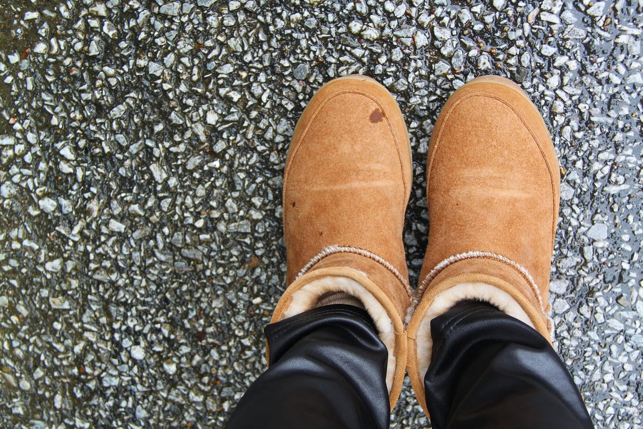 Tan sheepskin-lined suede boots with a small stain on one toe, on wet asphalt