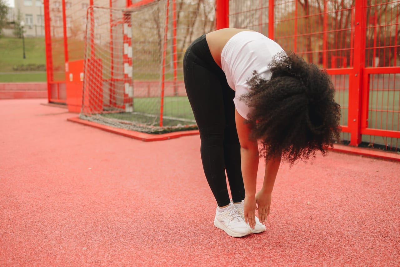 Woman in a standing forward fold, hands at her sneakers, on a red sports court