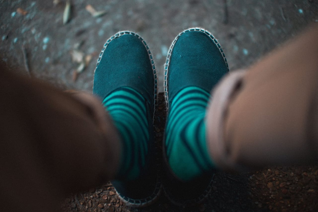Looking down at teal striped socks and dark green espadrilles on a gravel path