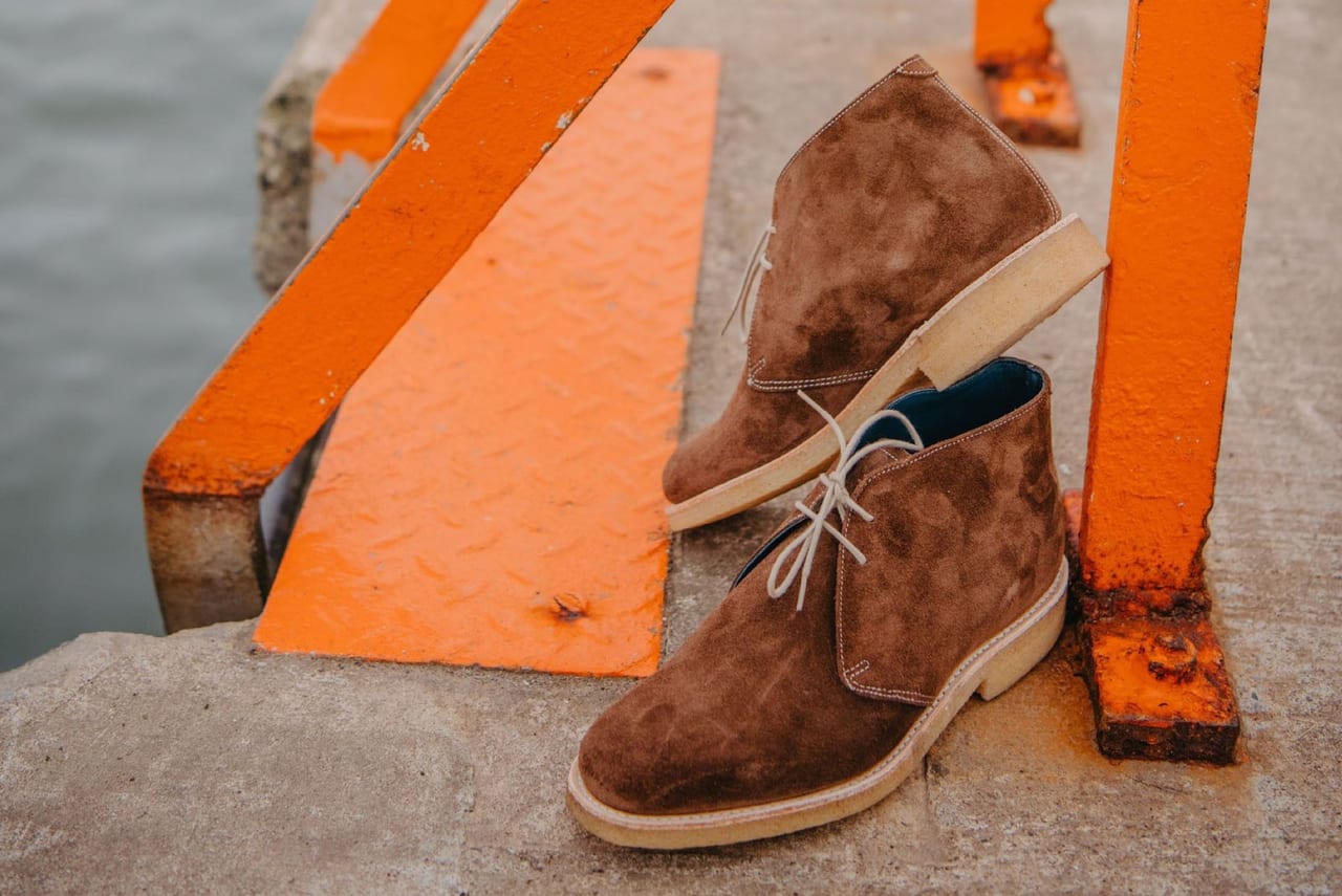 Pair of brown suede desert boots on concrete steps beside orange painted railings