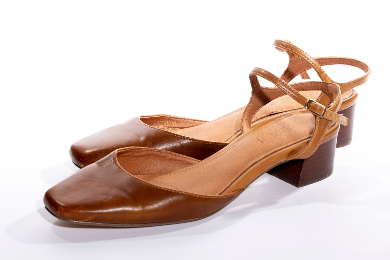 A pair of tan leather low block-heel shoes with square toes and ankle straps on white