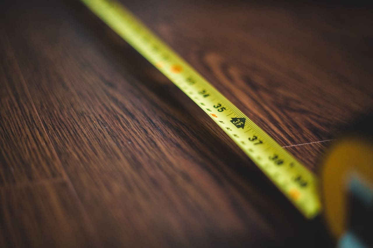 Yellow tape measure stretched across a dark wooden floor, its inch markings in focus