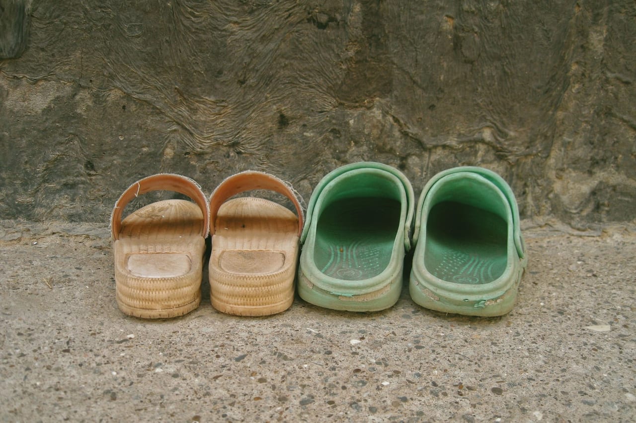 Two pairs of shoes, one woven slide and one green clog, side by side on concrete