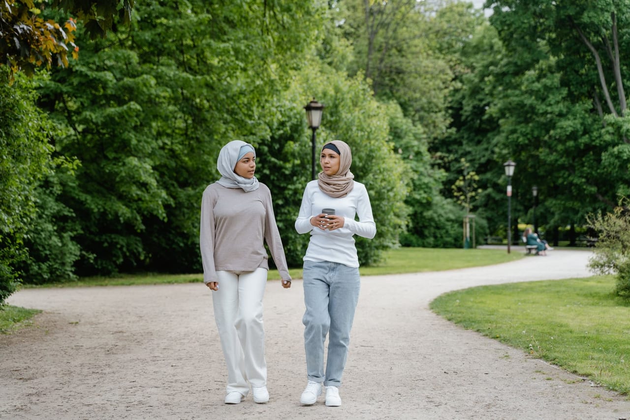 Two women in headscarves walking and talking side by side on a gravel park path