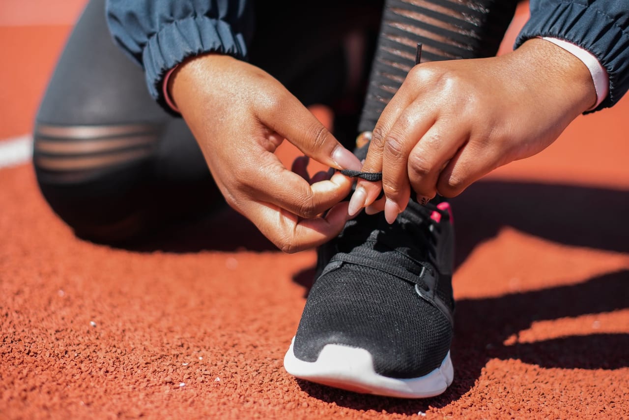Hands tying the laces of a black sneaker on a red running track