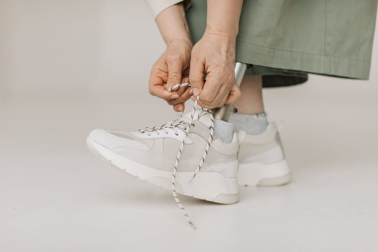 Hands tying the laces of cream chunky sneakers on a pale studio floor
