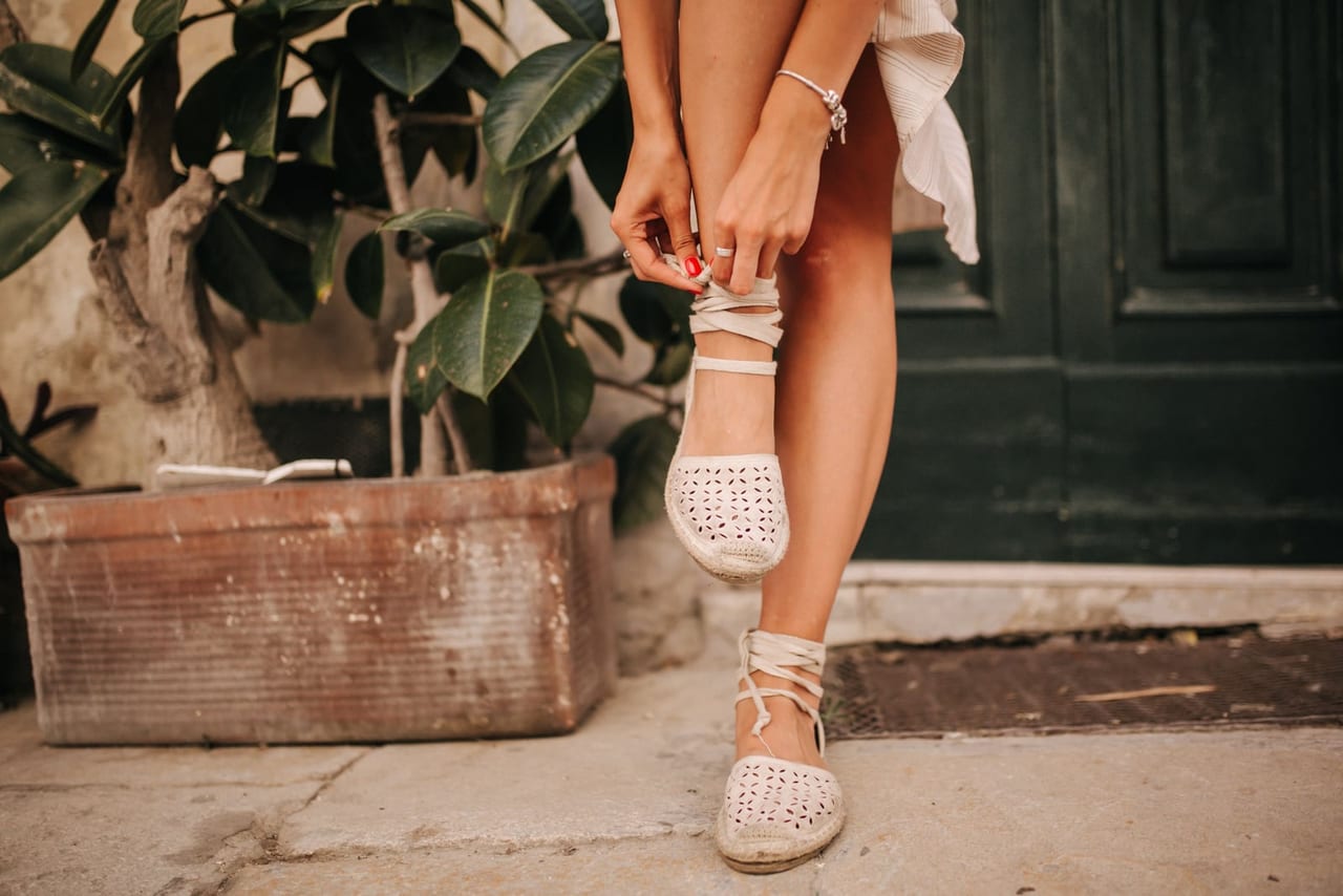 Woman tying the ankle straps of woven espadrille sandals on a sunny doorstep