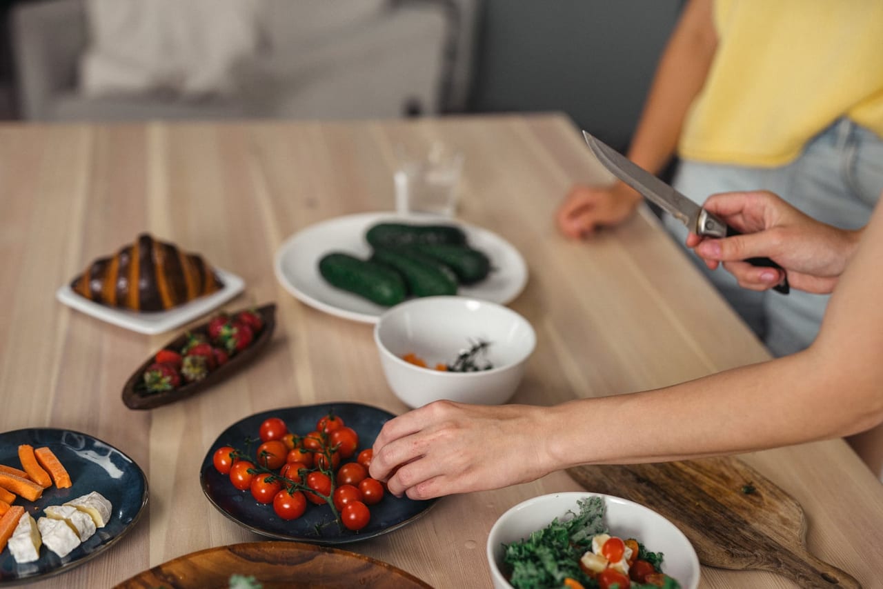 Hands setting out plates of cherry tomatoes, cucumbers, strawberries and greens on a wooden table