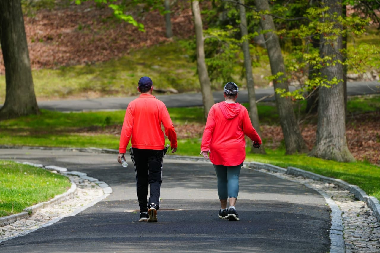 Two walkers in bright red tops heading along a paved path through a green park