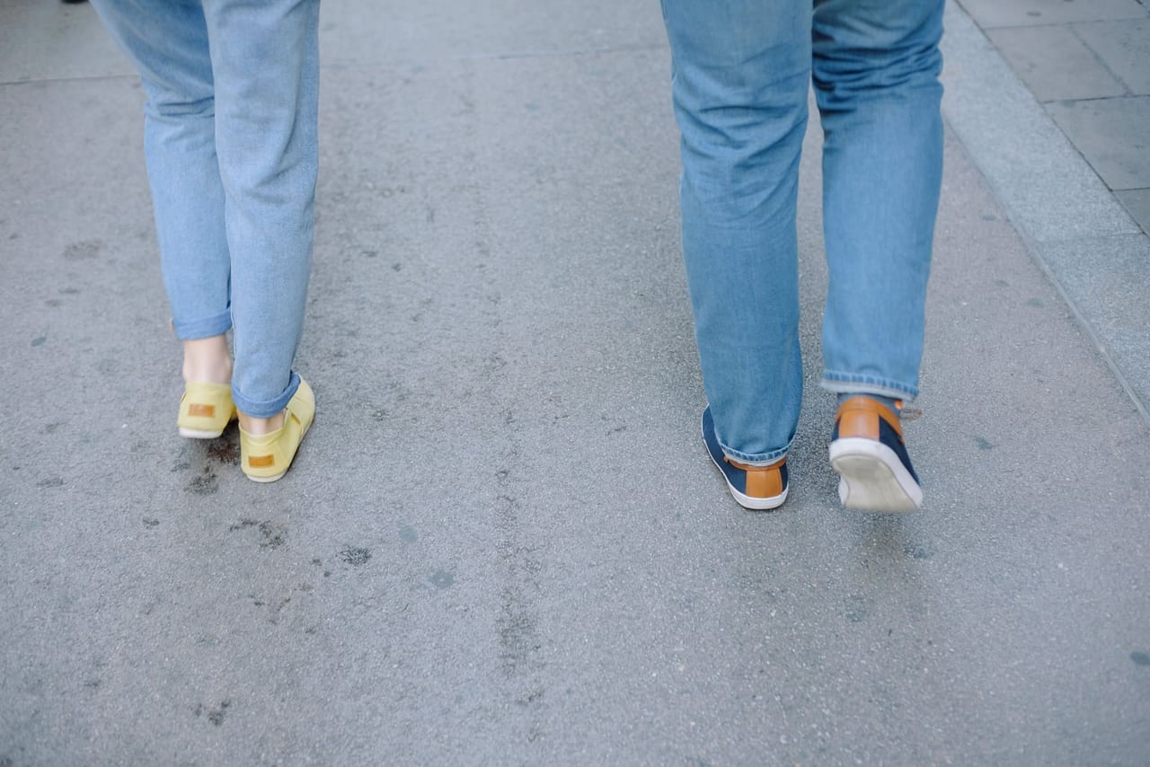 Two people in jeans and casual shoes walking side by side along a city sidewalk