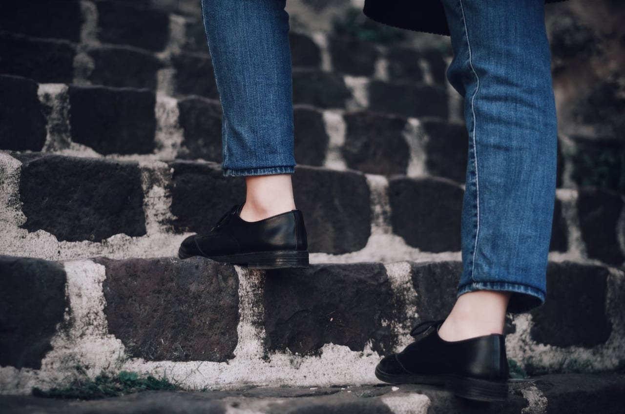 Legs in cuffed blue jeans and black leather shoes walking up dark stone steps
