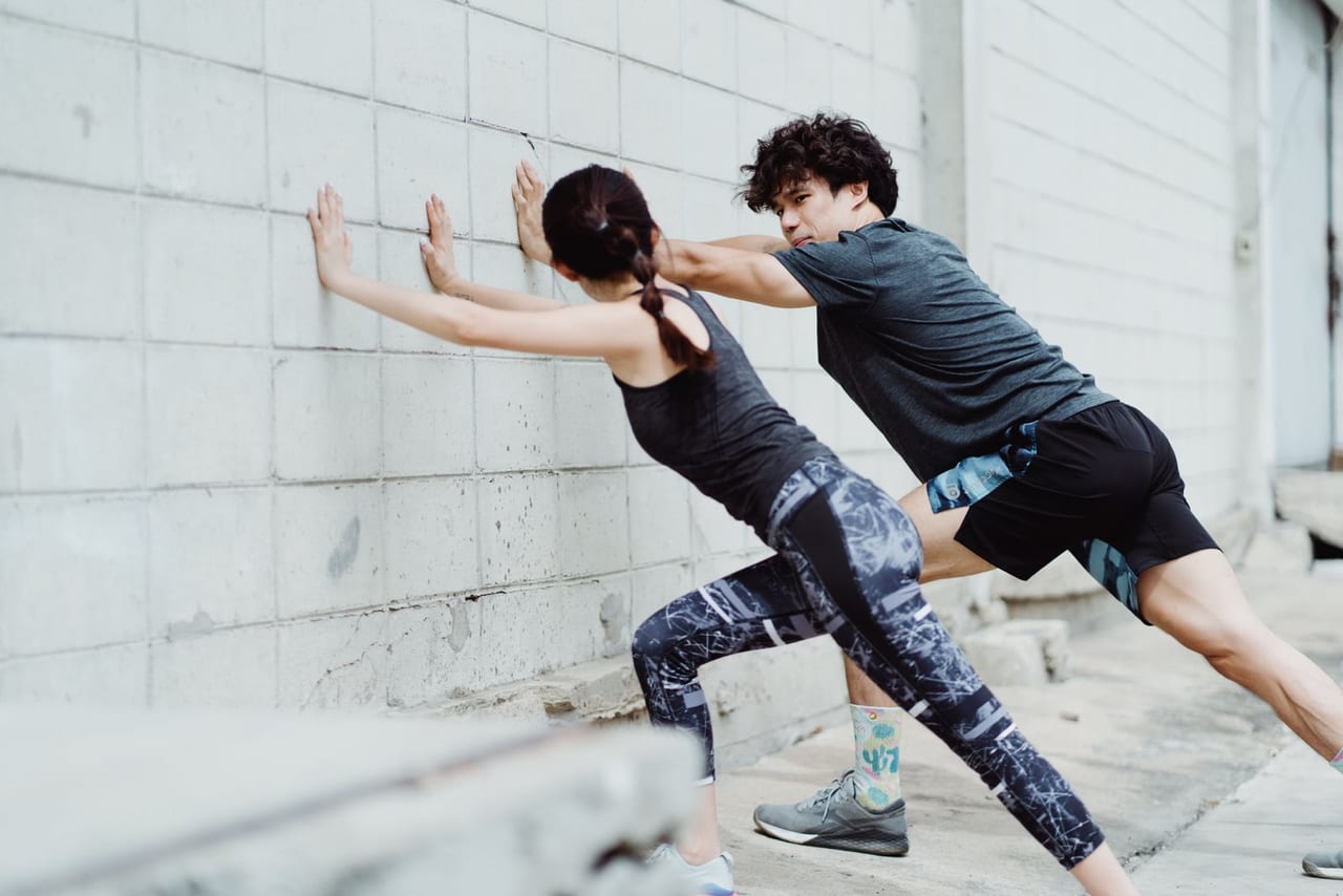 Man and woman leaning into a white brick wall with one leg stretched back