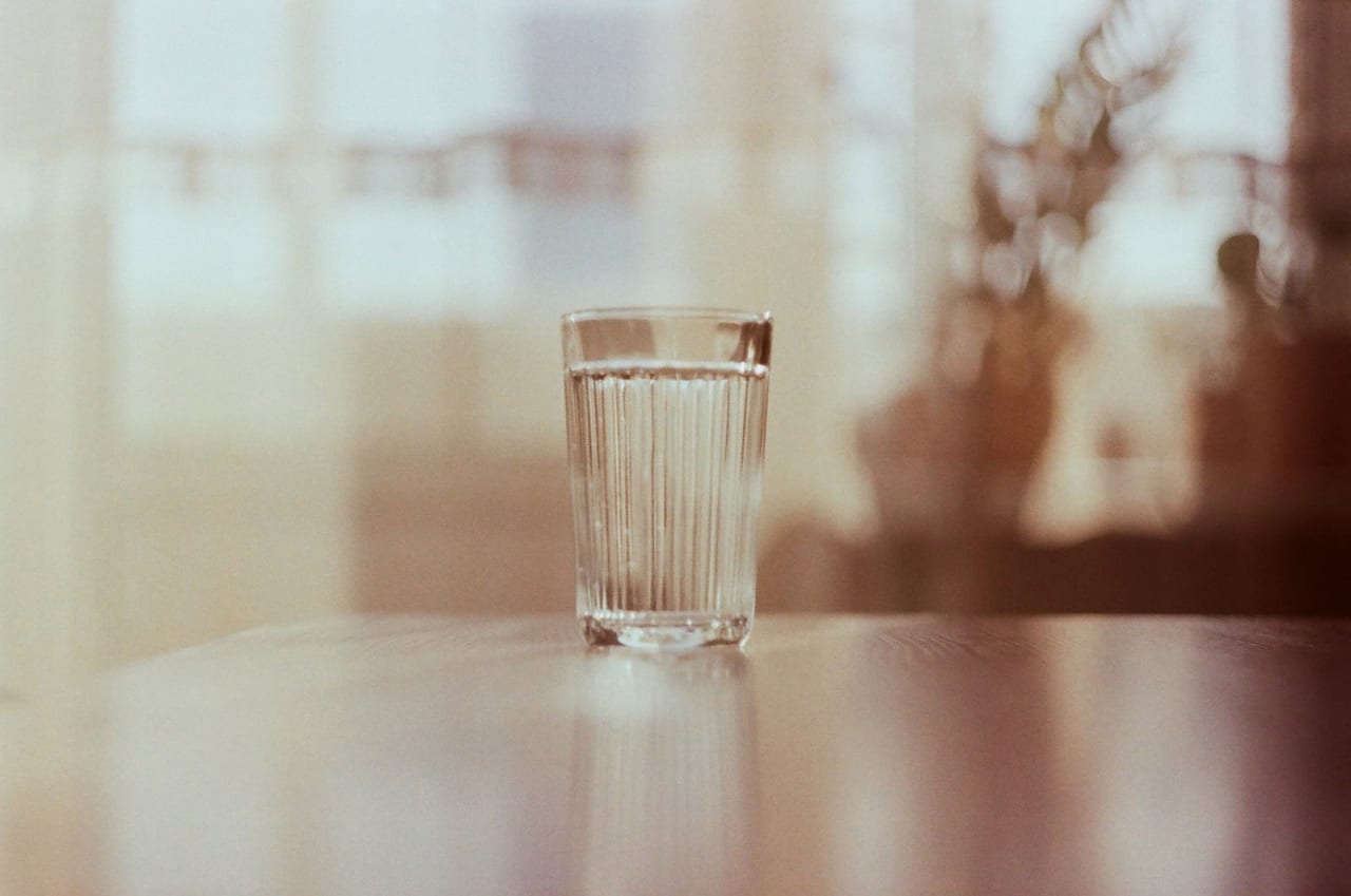 Ribbed glass of water on a wooden table in warm light by a window