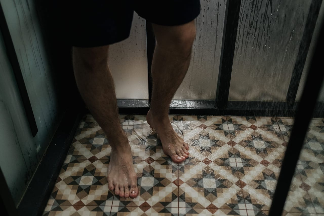 Bare feet standing on wet patterned floor tiles inside a glass shower stall