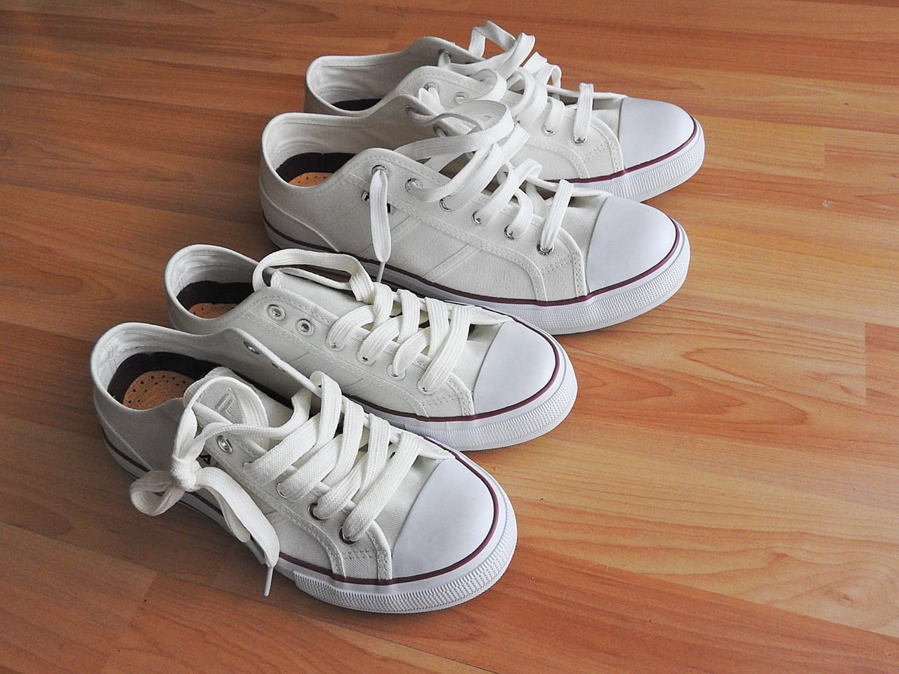 Two pairs of white canvas sneakers set in a row on a wooden floor