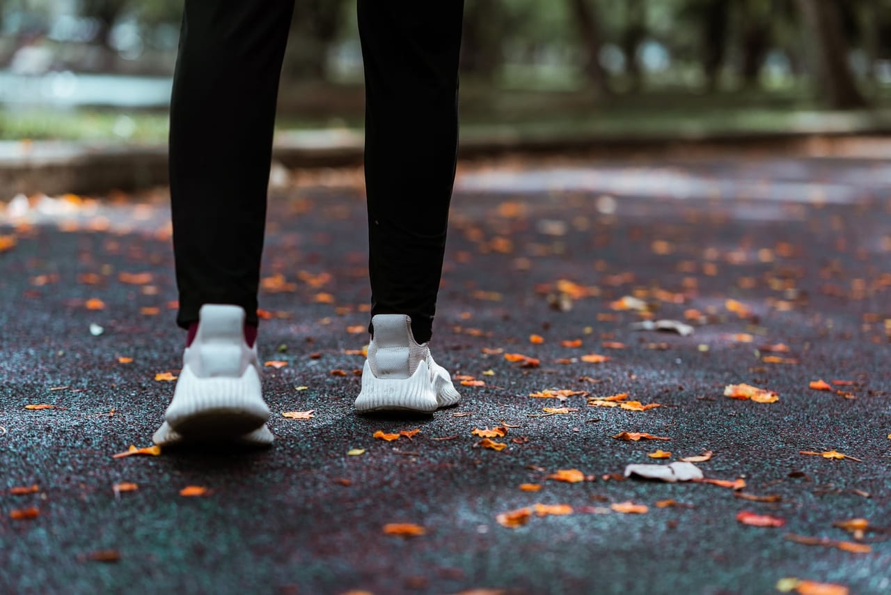 Back view of white sneakers and black leggings walking on a leaf-strewn park path