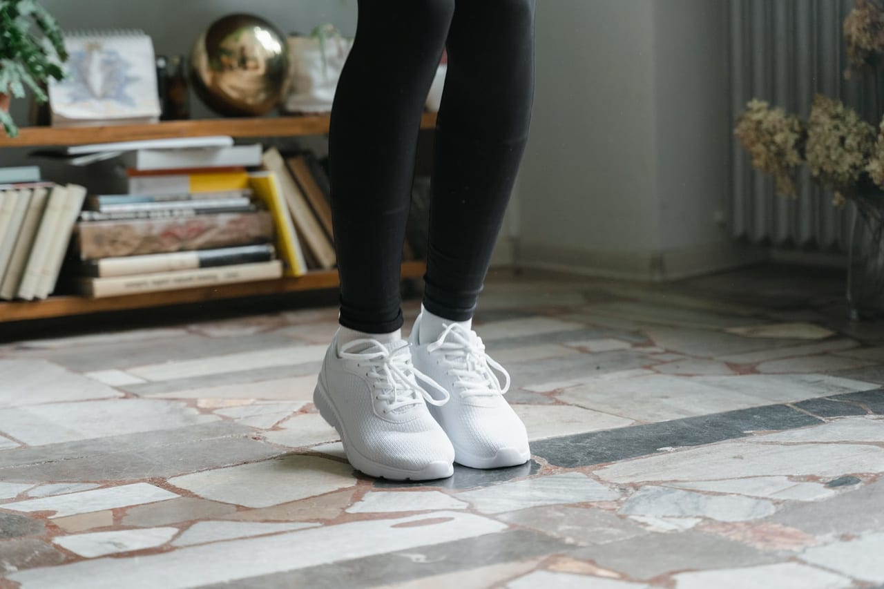 Person in black leggings, white socks and white lace-up sneakers standing on a stone floor