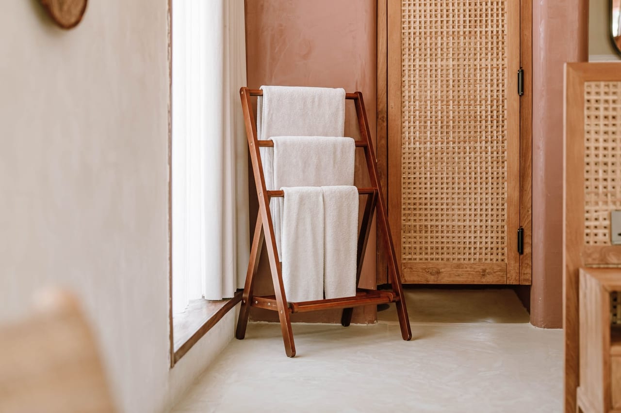 White towels folded over a wooden rack in a bright room beside a window